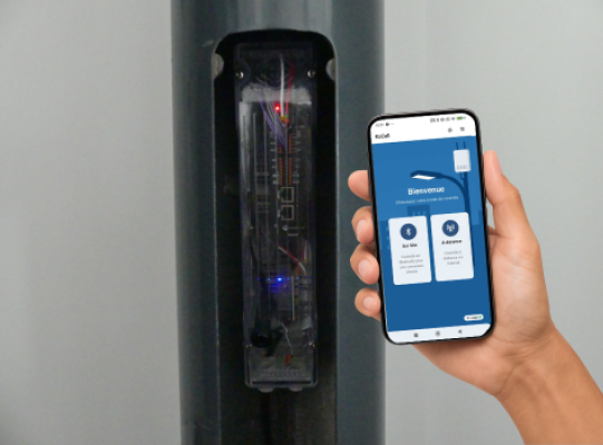 Trappe telecom de mât 5G ouvert laissant voir le connecteur Kocell à l'intérieur et une main tenant un téléphone avec l'appli dédiée